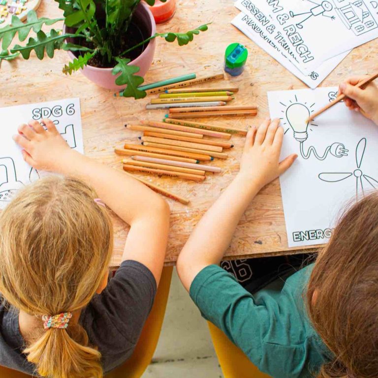 Kinder setzen Impuls malerisch um Zwei Kinder zeichnen auf Papier, umgeben von Bastelmaterial und einer Pflanze.
