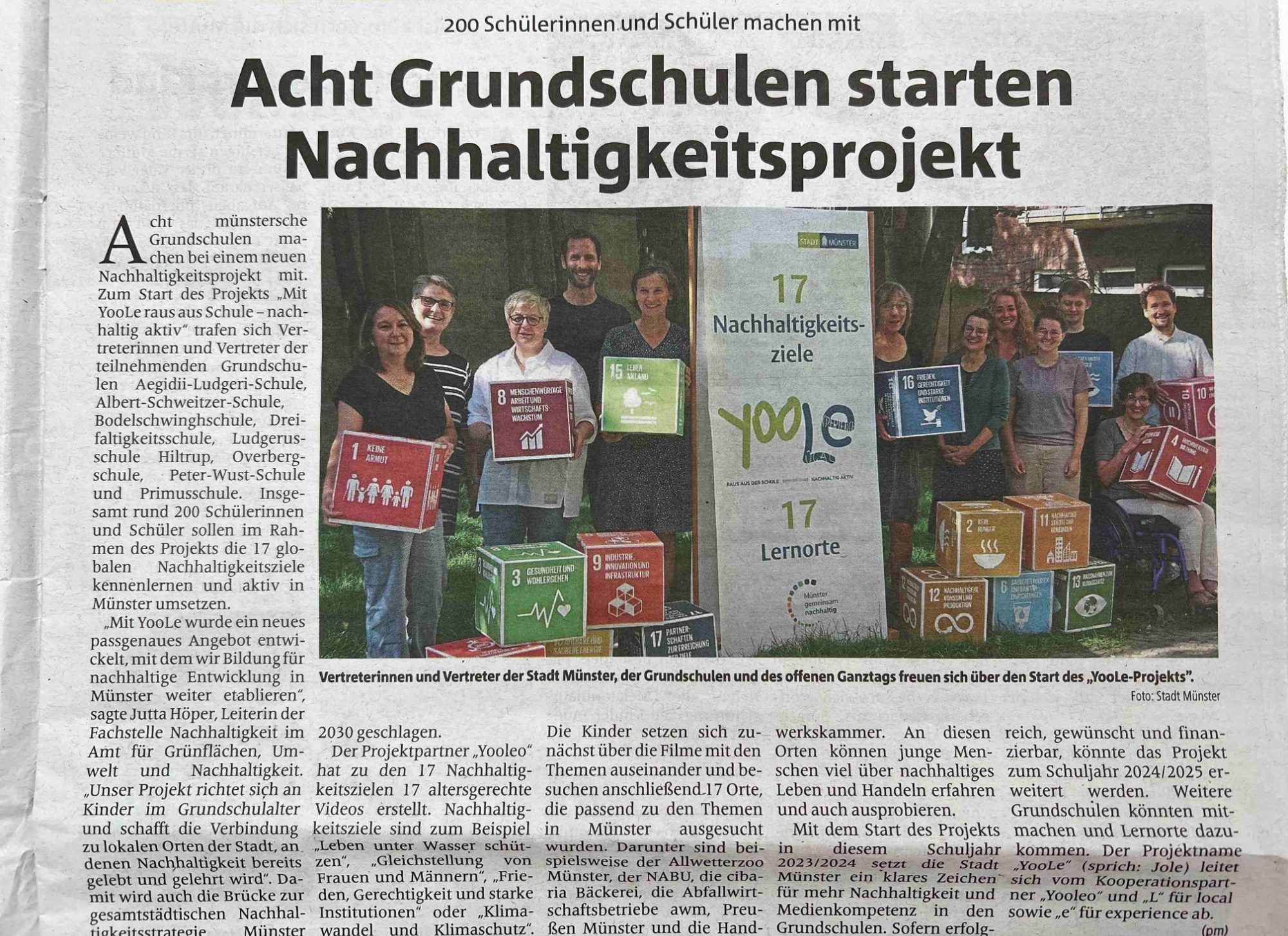 Stadt Münster setzt YOOLEO ein Zeitungsartikel aus Münster. Acht Grundschulen starten BNE-Projekt. 12 Personen stehen zusammen und zeigen die SDG-Ziele