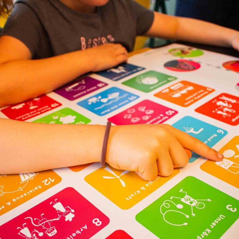 17 Nachhaltigkeitsziele Hände tippen auf ein buntes interaktives Lernspiel mit den 17 SDG-Symbolen.