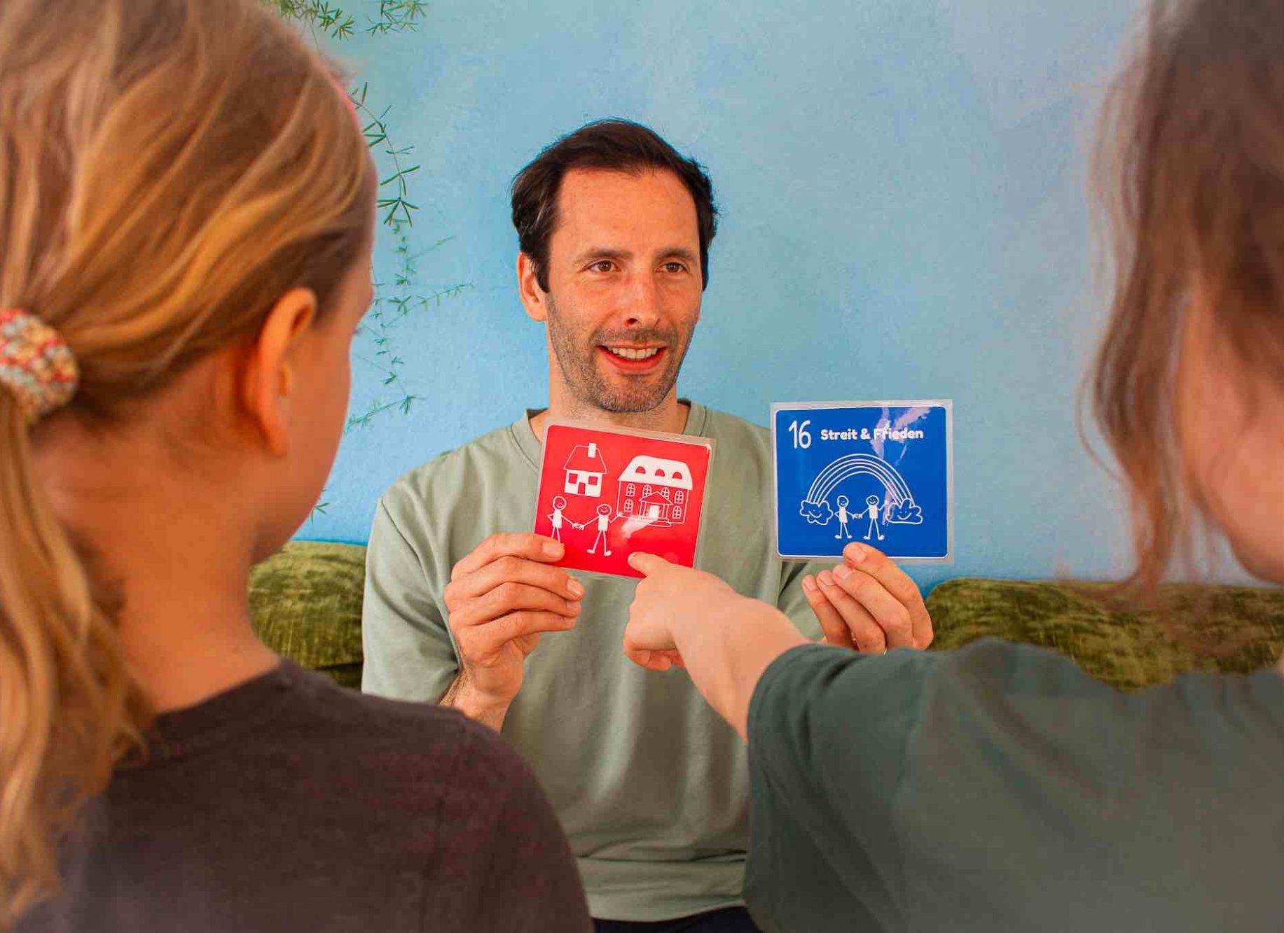 Themenauswahl für die YOOLEO-Inhalte Ein Mann hält rote und blaue Karten hoch, während zwei Kinder darauf zeigen.